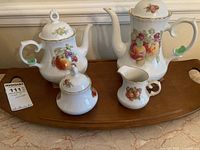 Full set on a wooden tray: coffee pot, teapot, creamer, sugar bowl with lids, all decorated with fruit and flower motifs and gold accents.