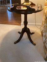 Full view of the round pedestal side table, showing tabletop, railings, pedestal and legs.