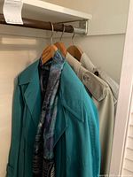 Two ladies spring coats hanging on wooden hangers, one turquoise Ladea coat with patterned scarf, one beige London Fog trench coat.
