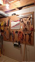 View of a pegboard with various hand tools including saws, pliers, drill, screwdrivers, scissors, level, and extension cords hung neatly on hooks