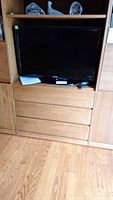 Samsung black flat screen TV, 32 inch, placed inside wooden shelving unit with remote on shelf below.