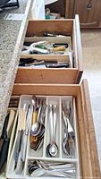 Top view of two open kitchen drawers containing assorted flatware and utensils including knives, forks, spoons, and various cutting tools.