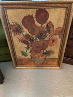 Framed Van Gogh "Sunflowers" print leaning against a green sofa and beside a wooden dresser, showing the full artwork and frame details.