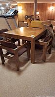 Photo of square wood dining table with four matching upholstered chairs around it, showing wood grain and general condition.