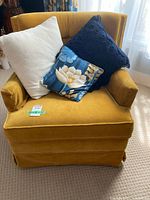 Front view of the vintage upholstered armchair with three pillows on the seat showcasing mustard yellow fabric and tufted back