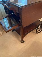 Side view showing the glass tray insert inside the wooden frame, a caster wheel, and the drop-leaf side down.