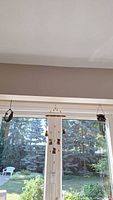 Three small wind chimes hanging in front of a window with outdoor view.