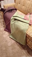 Two wool blankets draped over a couch, one maroon with pink trim, one greenish with pink trim and a Kenwood label visible.
