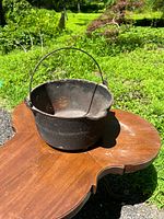 Top angle showing the antique cast iron pot with handle, heavy rust, placed outside on wooden surface