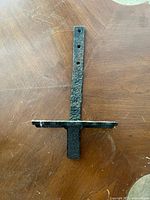 Top down angled view showing the textured metal strap with mounting holes extending vertically and the metal peg perpendicular at the base.