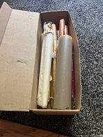 Box of assorted mixed color taper candles and one large beige pillar candle, showing contents inside the box.