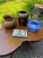 Clear overhead view of the four pottery items on a wooden table outdoors including pot, pitcher, vase, and tile.