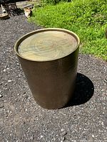 Full view of round brass outdoor table placed outdoors showing rust, discoloration, and scuffs on top and side surfaces.
