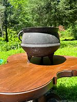 Cast iron cauldron showing profile and leg design on wooden surface outdoors in daylight.