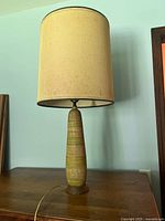 Full view of the ceramic lamp with shade on wooden table against light blue wall.