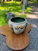 Photo of the pottery vase on a wooden table outside, showing shape and multicolored abstract exterior design.