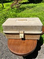 Closed fishing tackle box on wooden table outdoors.