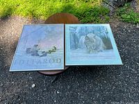 Two framed Robert Bateman prints on a round table outdoors, showing 'Iditarod' and 'Lynx' prints with signatures visible.