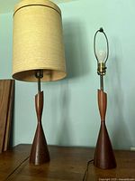 Two identical wood table lamps side by side, one fitted with beige drum shade