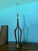 Full view of the mid-century modern table lamp showing wooden sculptural arms and gold-tone metal rod and socket.