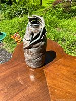 Photo of the pottery piece outdoors on wooden table showing its irregular folded shape and painted surface