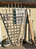 Two trellis panels leaning against a wall. One is fully assembled with pointed finials and horizontal slats, mocha color. Second trellis is unopened in its original cardboard packaging with label visible.