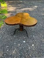 Full view of the clover-shaped wooden coffee table showing the top surface and overall shape, placed outdoors on gravel ground.