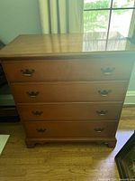 Front view of wood dresser showing four drawers and metal handles.