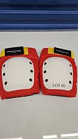 Front view of two knee protection pads showing red fabric and white plastic hard protective plate with rivets