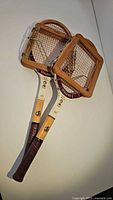 Two vintage wooden tennis rackets stacked on a flat surface, showing overall condition and length.