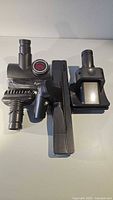 Three Dyson vacuum cleaner attachments laid out on a flat surface; motorized brush head, dusting brush, and crevice tool visible
