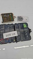 Black multi-compartment plastic tackle box open showing various fishing tackle accessories including hooks, swivels, clips, and beads along with a label Lot 118 on it.