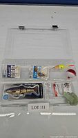 Clear plastic tackle box with various fishing hooks, lures, bobbers, and accessories inside.