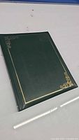 Photo album closed showing dark green hardcover with gold decorative border on front.