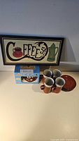 Photo showing coffee sign, four ceramic cups, and four matching saucers on a table.