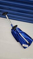 Two blue Michelin snow shovels laid on the floor, showing the full length including handles and blades.