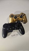 Two PlayStation controllers, one black and one gold, placed on a white surface with LOT 35 label.