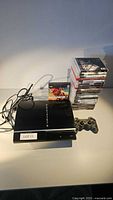Full lot shot showing PlayStation 3 console, controller, power cable, Max Payne 3 game case, and large stack of game cases