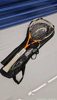 Two squash racquets in bags. One Head brand with orange and black details, the other a different brand racquet.