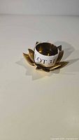 Front angle view of vintage brass gold candle holder shaped like a lotus flower with label Lot 31 inside.