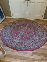 Full view of 6-foot round rug with red-centered intricate floral and geometric patterns in red, blue, beige, and green.