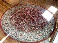 Full view of the 8' round rug with rustic red center and cream border on hardwood floor, showing overall condition and pattern.