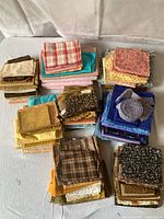 Multiple stacks of folded fabric pieces in various colors and patterns, including plaids, florals, abstract designs, and solid hues.