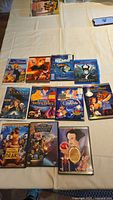 Full view of all 11 Disney animated movie DVDs laid out on cream-colored cloth, showing colorful covers including The Emperor's New Groove, The Lion King, Atlantis, Beauty and the Beast, Brother Bear, Finding Nemo, Sleeping Beauty, Cinderella, Treasure Planet, Snow White and the Seven Dwarfs, and Maleficent.