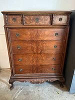 Front view of antique chest showing 3 small top drawers and 4 large main drawers with ornate carved details and metal ring handles.