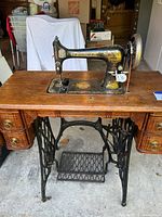 Full view of antique Singer treadle sewing machine mounted on wooden table with metal treadle base and drawers on both sides.