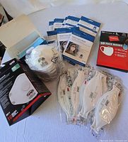 Photo content showing assortment of 3M N95 masks, KN95 masks in blue and white boxes, and Hanes cloth masks in red box