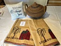 Photo showing woven basket with lid, small decorative pillow with embroidered text, and two window valances with country motif laid flat on table
