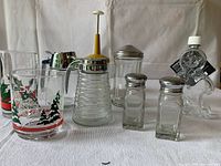 Photo showing vintage glass honey dispenser, syrup pitcher, sugar pourer, salt and pepper shakers, and nut chopper with Christmas tree mug in background.