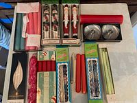 Photo of assorted taper candles including boxed Alaska souvenir candles, novelty Santa candles, stainless steel candle holders, and various other colored candles.